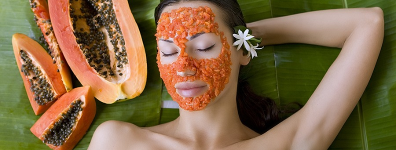 woman laying next to a large papaya with tiny papaya pieces on her face