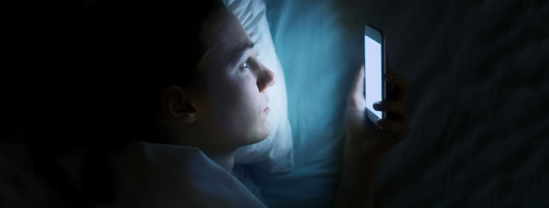 man looking at his phone in the dark in bed. 